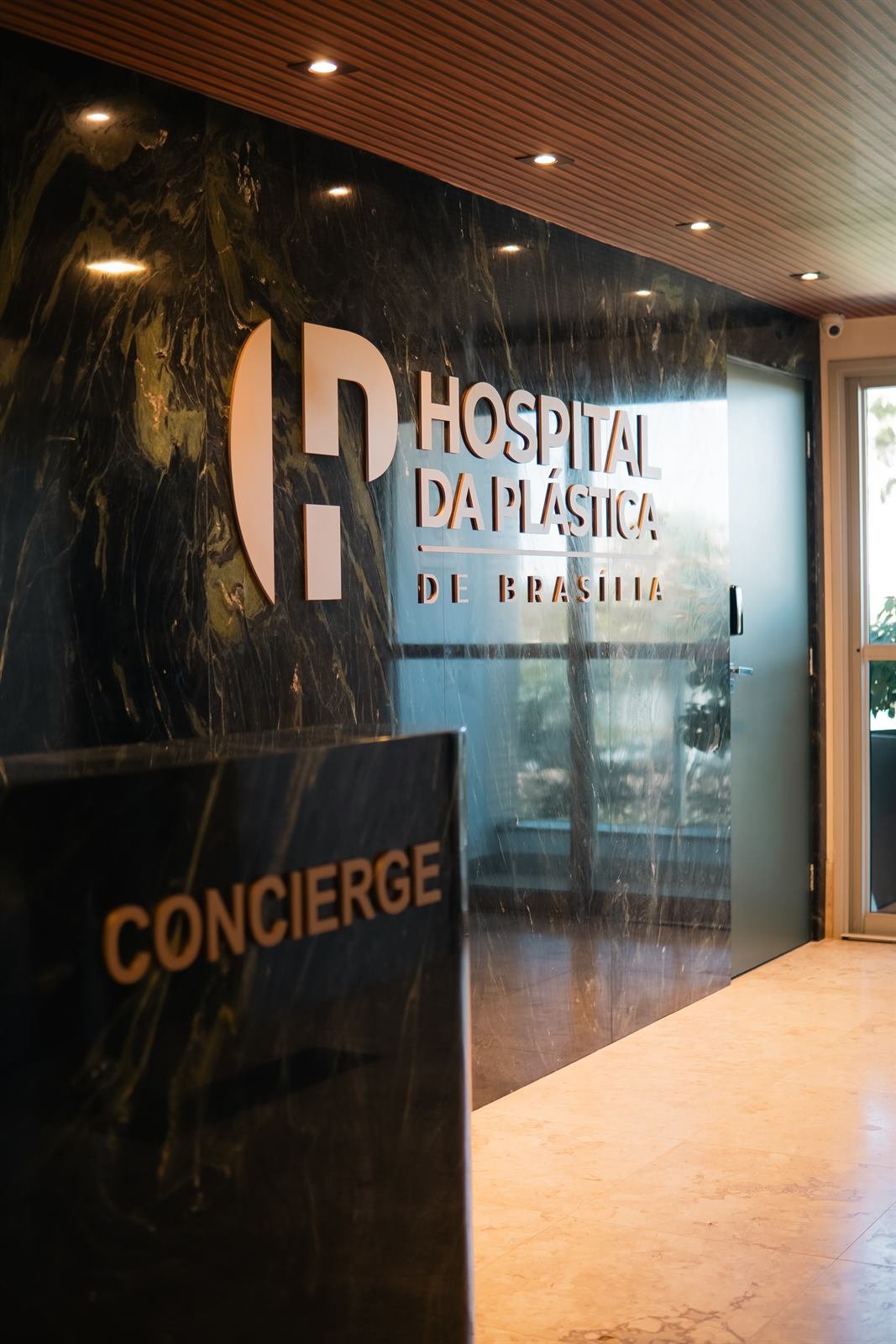 Recepção do Hospital da Plástica de Brasília com concierge e logotipo em parede de mármore